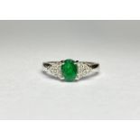 An emerald and diamond cluster ring, the central oval-cut emerald claw-set between shoulders mounted