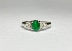 An emerald and diamond cluster ring, the central oval-cut emerald claw-set between shoulders mounted