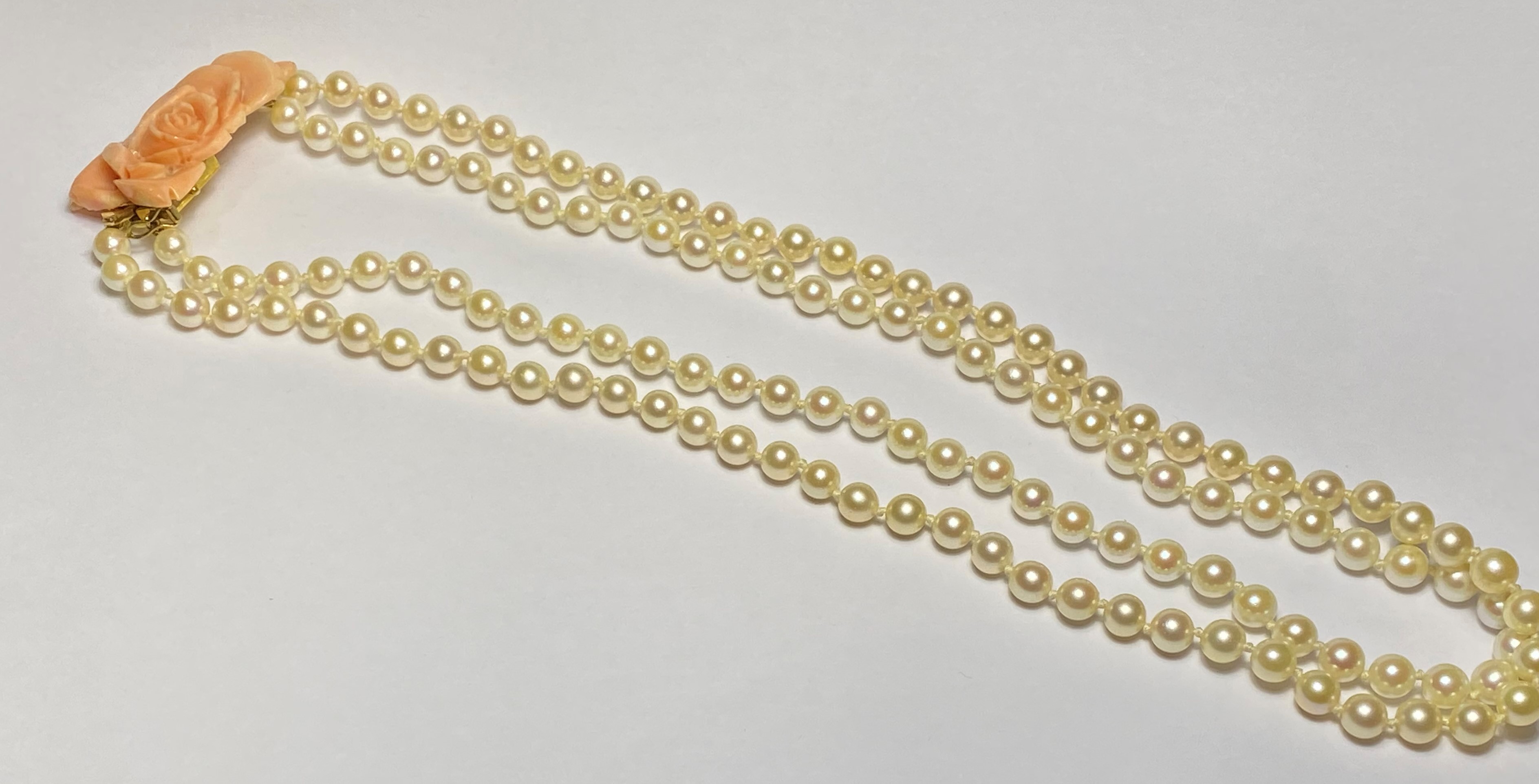 A double strand of uniform cultured pearls on a coral clasp carved as a rose and mounted in 9ct