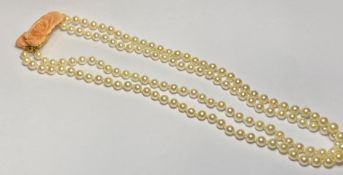 A double strand of uniform cultured pearls on a coral clasp carved as a rose and mounted in 9ct