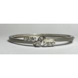 An 18ct white gold, diamond-set bangle, the hinged oval bangle claw-set with twin bands of three