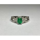 An emerald and diamond cluster ring, the central oval-cut emerald claw-set on split shoulders set