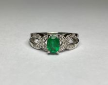 An emerald and diamond cluster ring, the central oval-cut emerald claw-set on split shoulders set