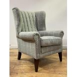 Anta, a barrel back wing armchair, upholstered in tartan wool enriched with studded detail, raised