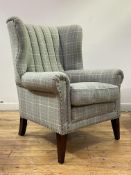 Anta, a barrel back wing armchair, upholstered in tartan wool enriched with studded detail, raised