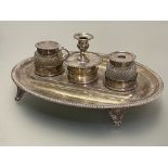 An early 19th century silver desk standish, the oval stand with gadrooned edge and raised on