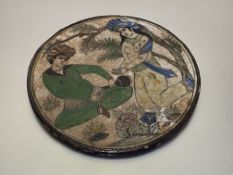 A large Qajar style pottery tile, circular, painted with a seated male figure beside a female