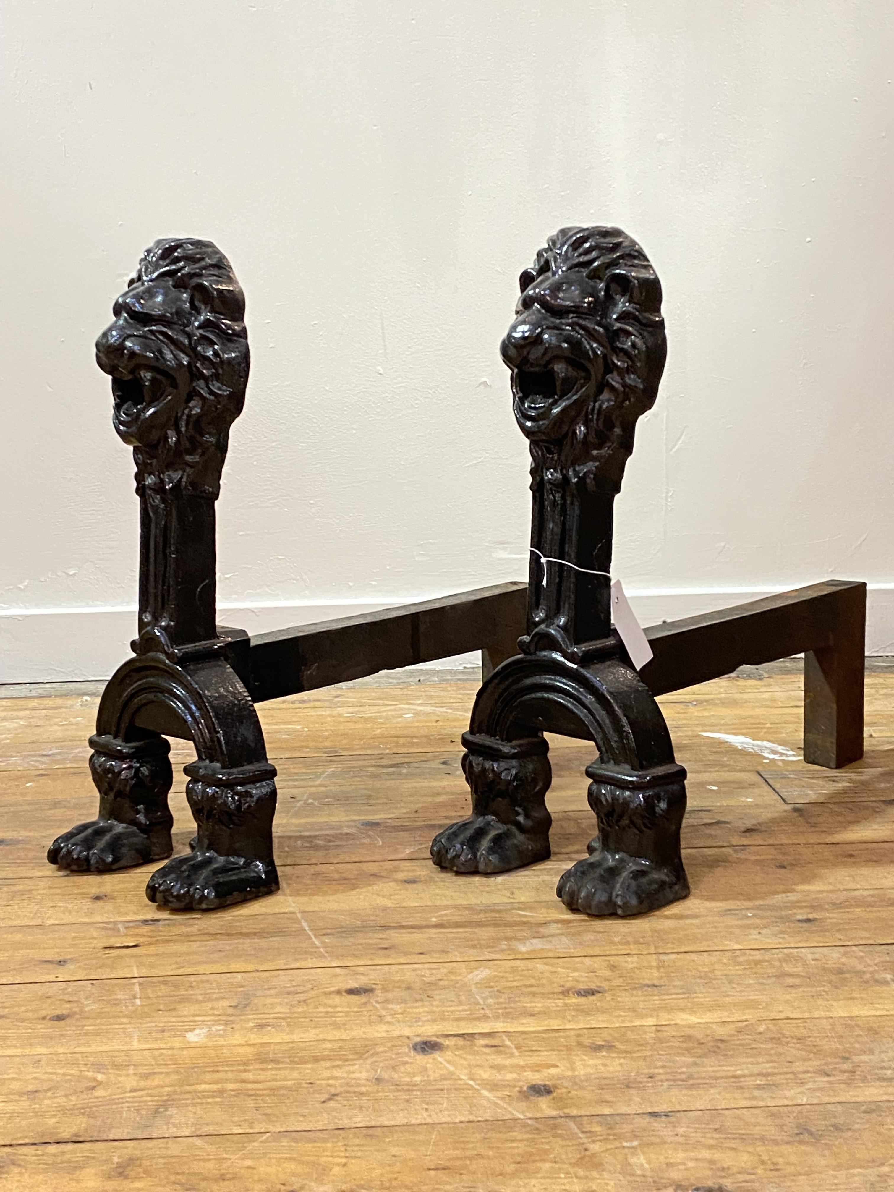 A pair of imposing cast iron andirons, each with a lion mask surmount over paw feet, H52cm, L53cm,