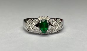 An emerald and diamond cluster ring, the central oval-cut emerald claw-set on a shaped plaque of