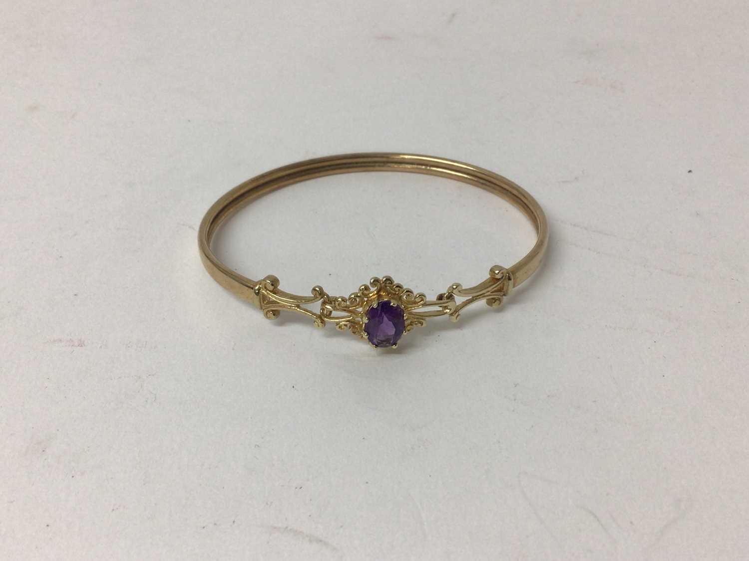 9ct gold and amethyst bangle with an oval mixed cut amethyst and gold scroll shoulders.