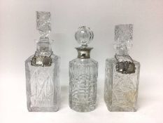 Two square cut glass decanters with silver labels, and another decanter with silver collar