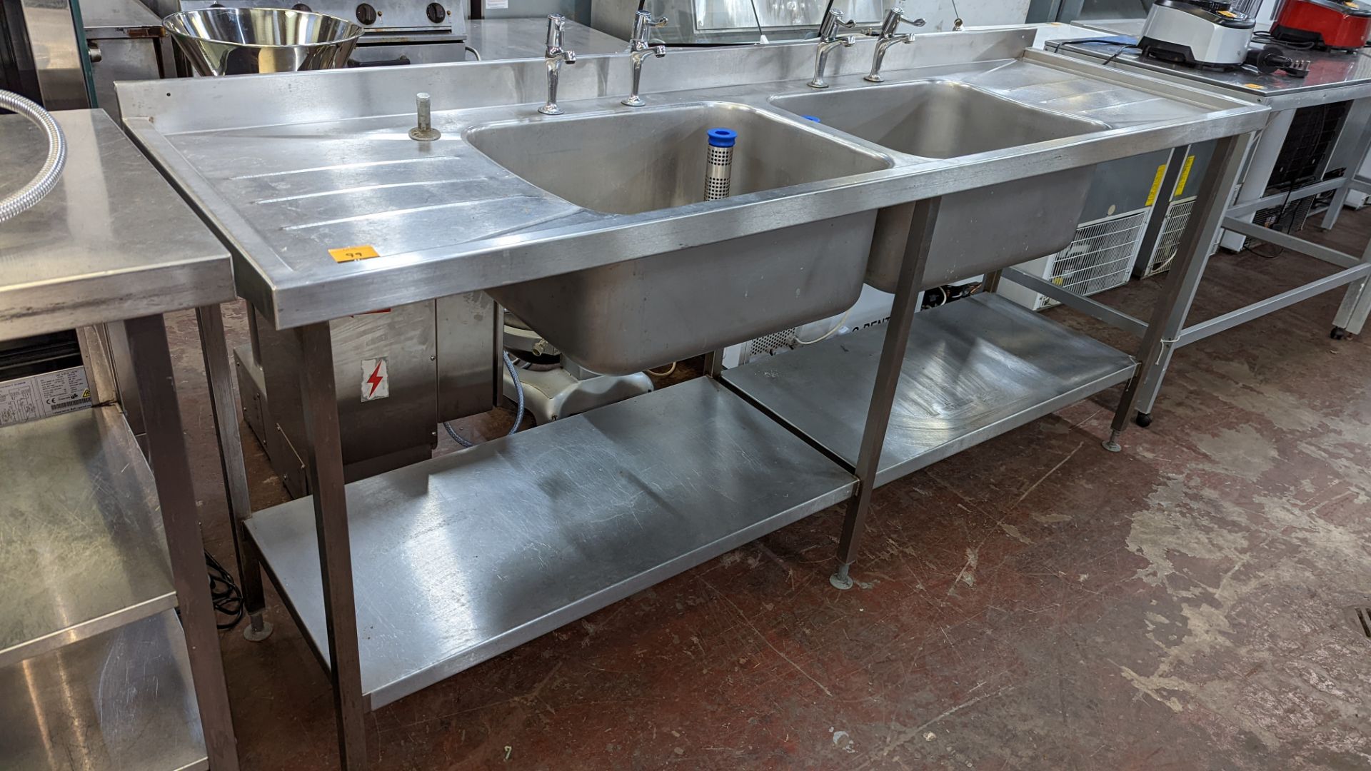 Large stainless steel twin bowl sink arrangement incorporating taps, drainers & shelves below, max e