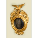 An impressive gilt wooden eagle-topped mirror with ebonised inner medallion, 19th C.