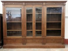 LARGE CARVED OAK BOOKCASE having detail to the frieze over four glazed doors and interior adjustable