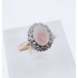 9CT GOLD OPAL & DIAMOND OVAL CLUSTER RING, the cabochon opal surrounded by a row of tiny diamonds,