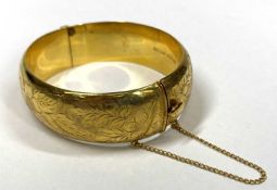 9CT GOLD HOLLOW CORE BANGLE WITH SAFETY CHAIN - with full foliate outer decoration, circa 1970s,