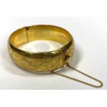 9CT GOLD HOLLOW CORE BANGLE WITH SAFETY CHAIN - with full foliate outer decoration, circa 1970s,