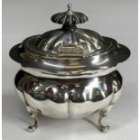 AN OVAL SILVER TEA/SUGAR CADDY - with single hinged lid and on four scrolled supports, fine clear