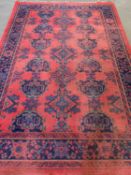 EASTERN STYLE WOOLLEN RUG, red ground with repeating central pattern and blue border, 305 x 204cms