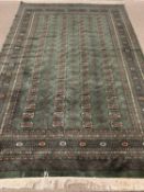 GREEN GROUND RUG with multiple pattern border and four central rows of repeating motifs, 290 x