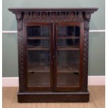 STAINED OAK TWO-DOOR GLAZED LOW-COUNTRY BOOKCASE, heavily carved with carved mask corbels, 115cms