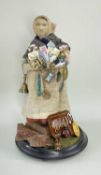 FEMALE PEDDLER DOLL, with cloth body, dressed in headscarf, shawl, apron and skirt, selling a
