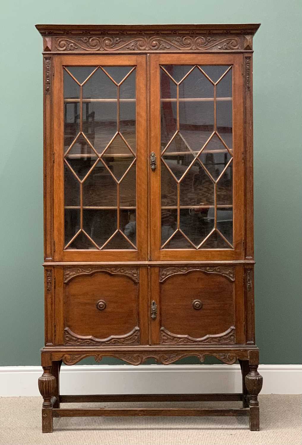 AN OAK EDWARDIAN BOOKCASE CUPBOARD - with carved detail, astragal type glazed twin doors, two