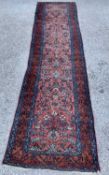 AN EASTERN WOOLLEN CARPET RUNNER - red ground with central floral pattern and triple bordered