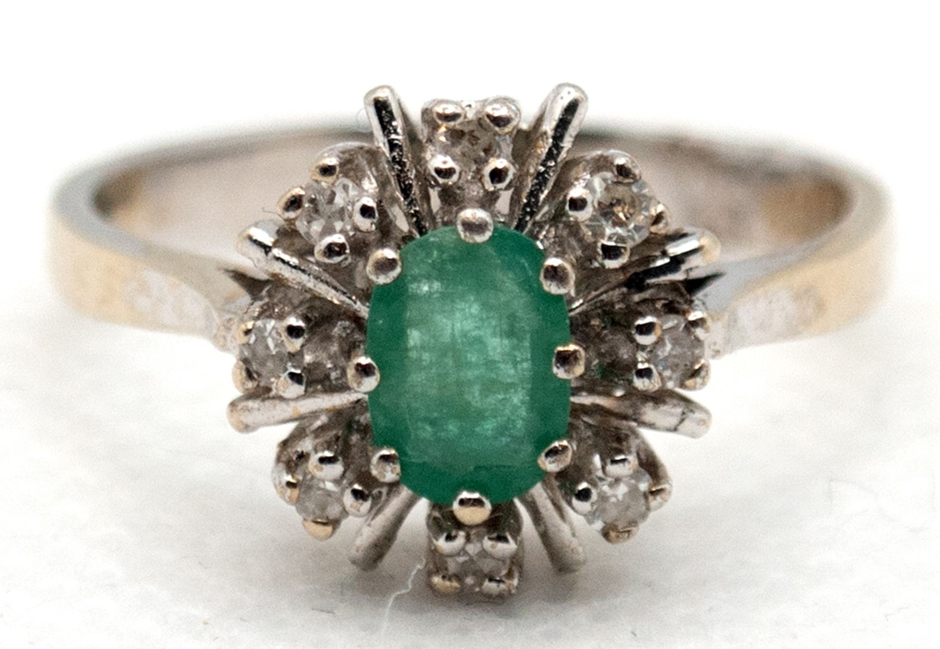 Ring, 585er WG, besetzt mit oval facettiertem Smaragd, der von 8 Brillanten von zus. ca. 0,08 ct. u