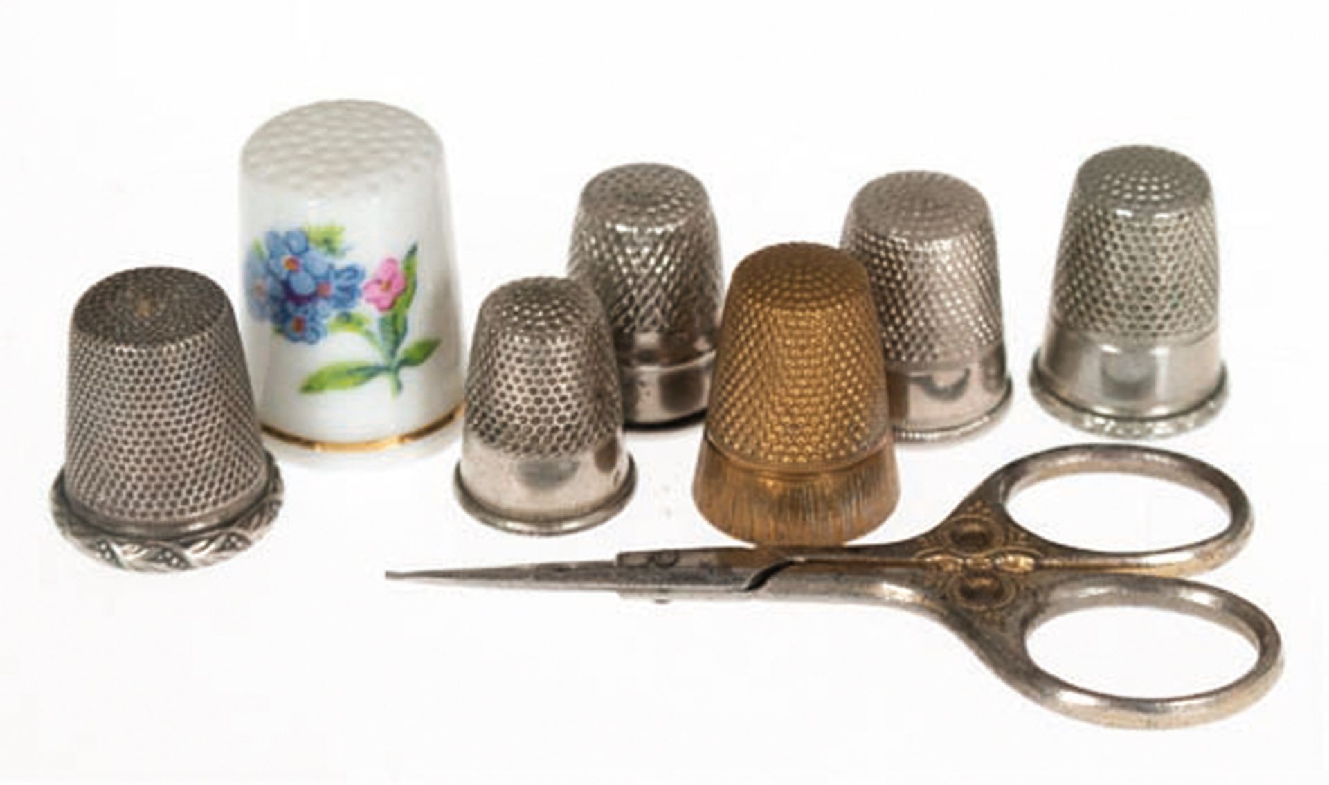 7 Fingerhüte und Schere, 1 x Porzellan mit floralem Dekor und Goldrand, 6x versilbert, versch. Größ