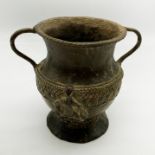AN UNUSUAL EARLY METAL URN WITH GREEK INSPIRED PATTERN IN FIGURES IN SEATING POSITION ON EACH SIDE