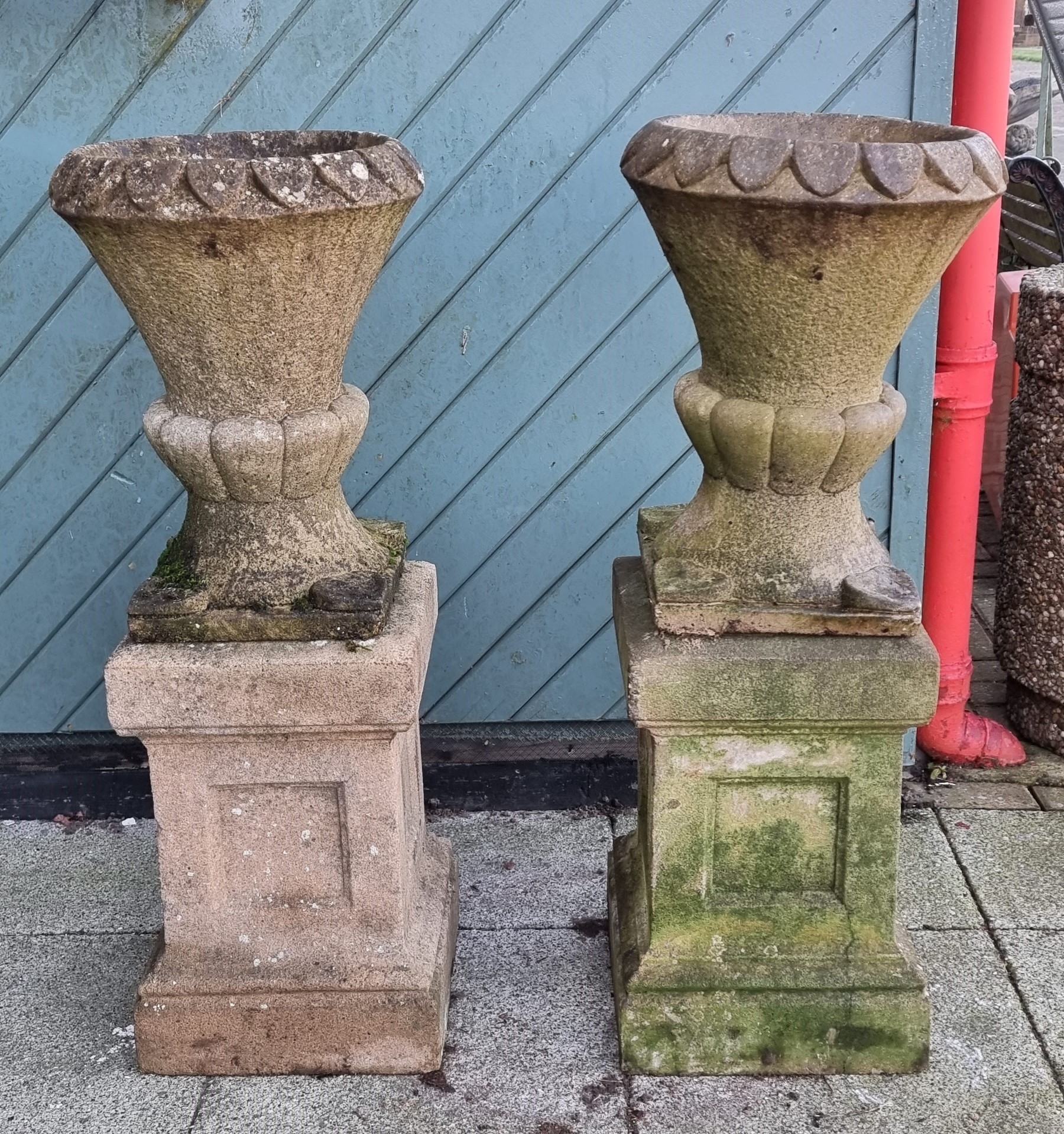 A pair of reconstituted stone garden urns, raised on square plinths, 96cm