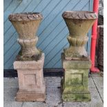 A pair of reconstituted stone garden urns, raised on square plinths, 96cm