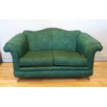 A two seater chesterfield style sofa, upholstered in floral emerald green fabric, raised on brass