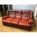 A three seater chesterfield sofa, upholstered in rouge red hide/leather, button back decoration. L16