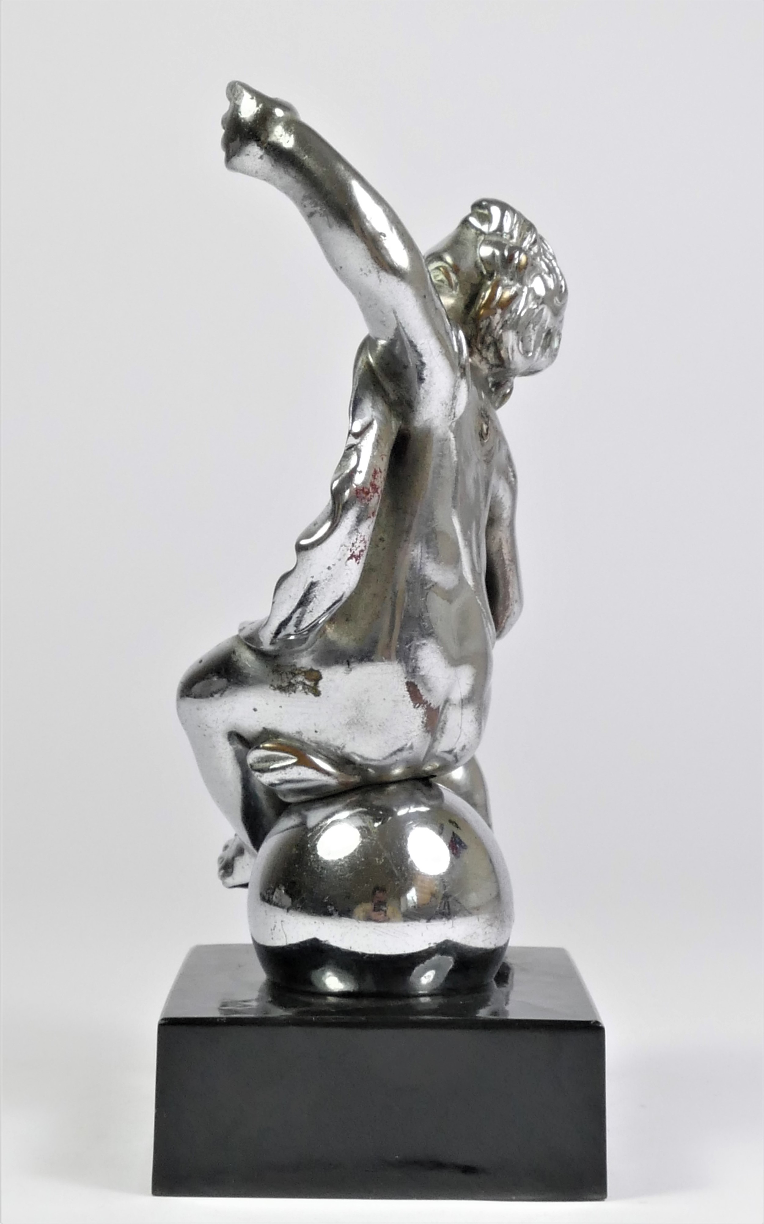 A chrome car mascot in the form of a cherub seated on a ball, mounted on a black onyx base, 18cm. - Image 2 of 2