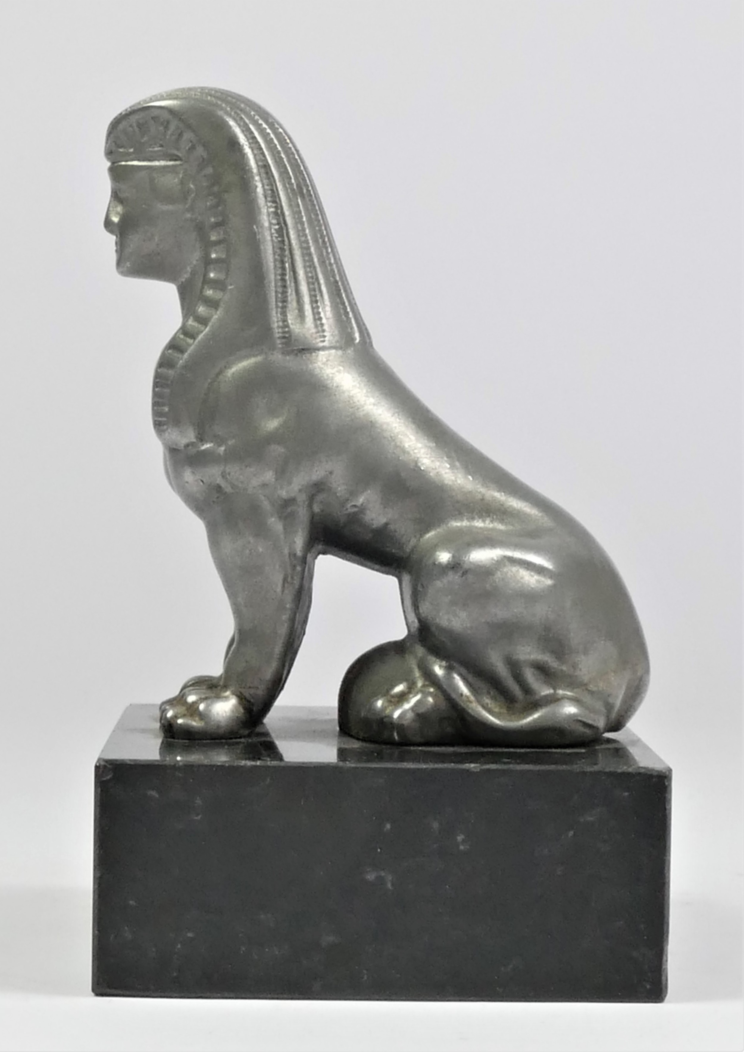 A base metal car mascot in the form of a seated Sphynx mounted on a black onyx base, 11cm.