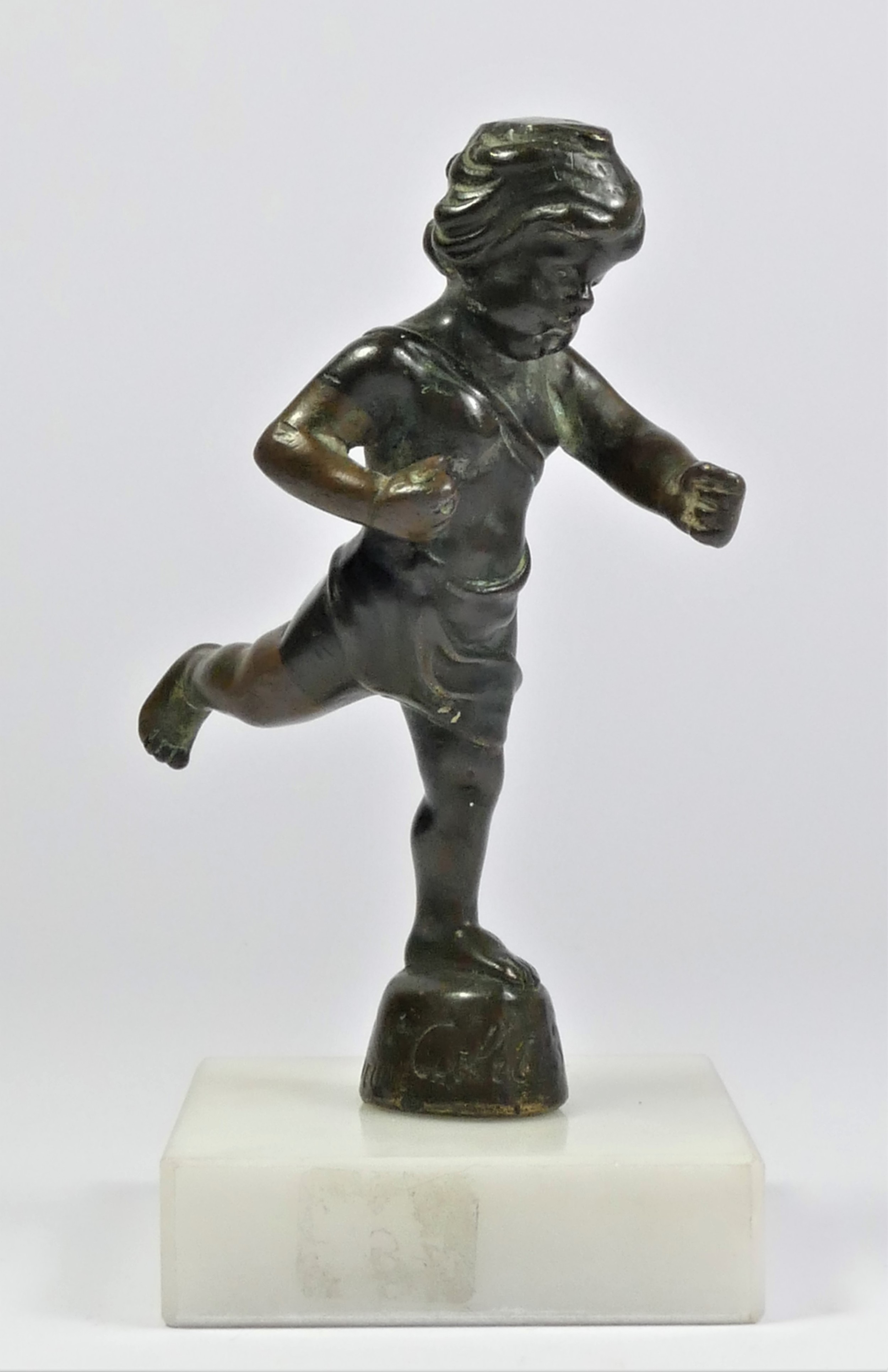 A bronze cherub car mascot signed Cubitt Cupid by Emile Lejeune, mounted on a white marble base,