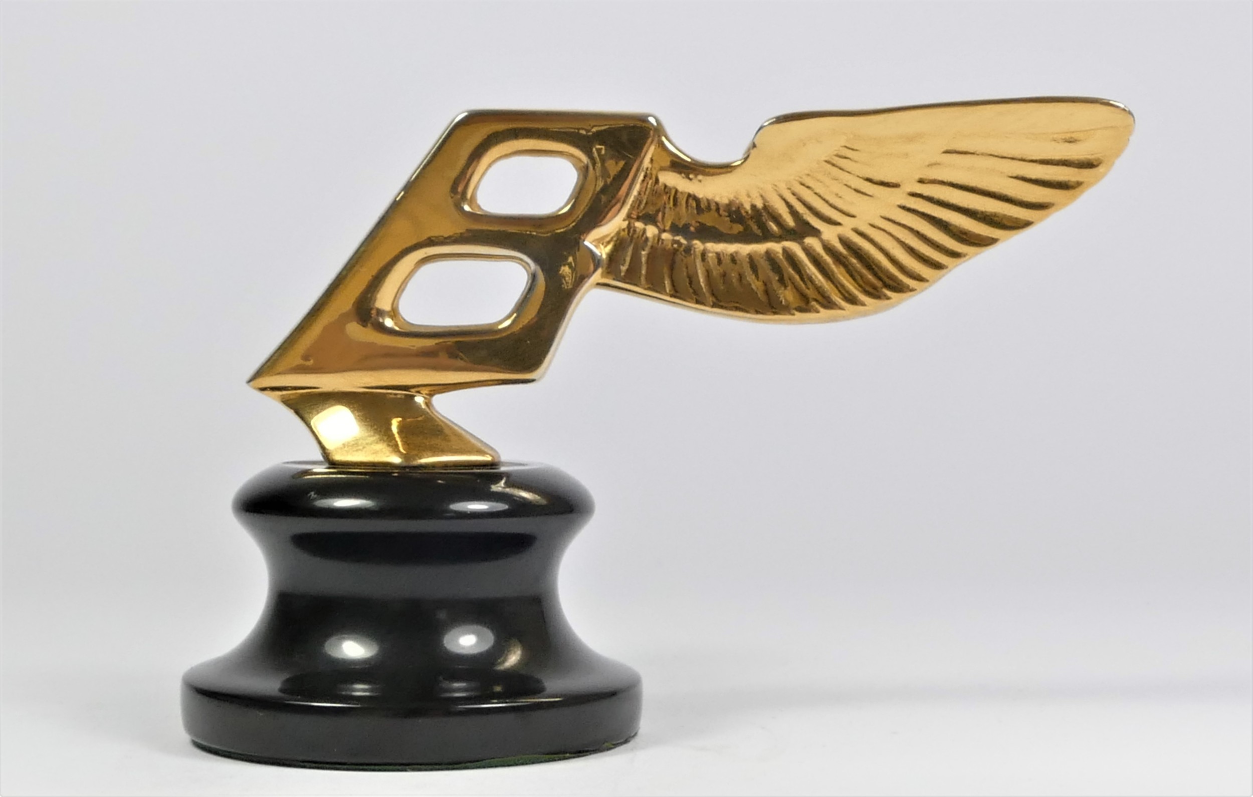 A gold plated car mascot in the form of a winged Bentley mounted on a black base, 9cm.