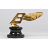A gold plated car mascot in the form of a winged Bentley mounted on a black base, 9cm.