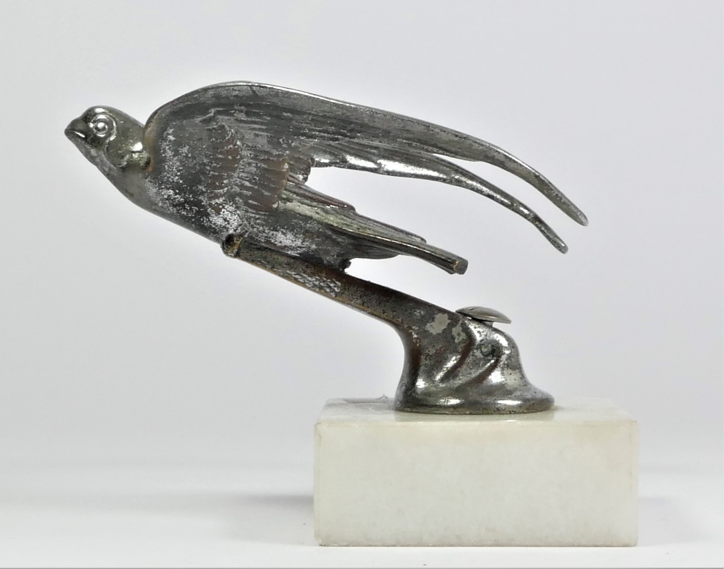 A chrome car mascot in the form of a flying swift mounted on a white onyx base, 10cm.