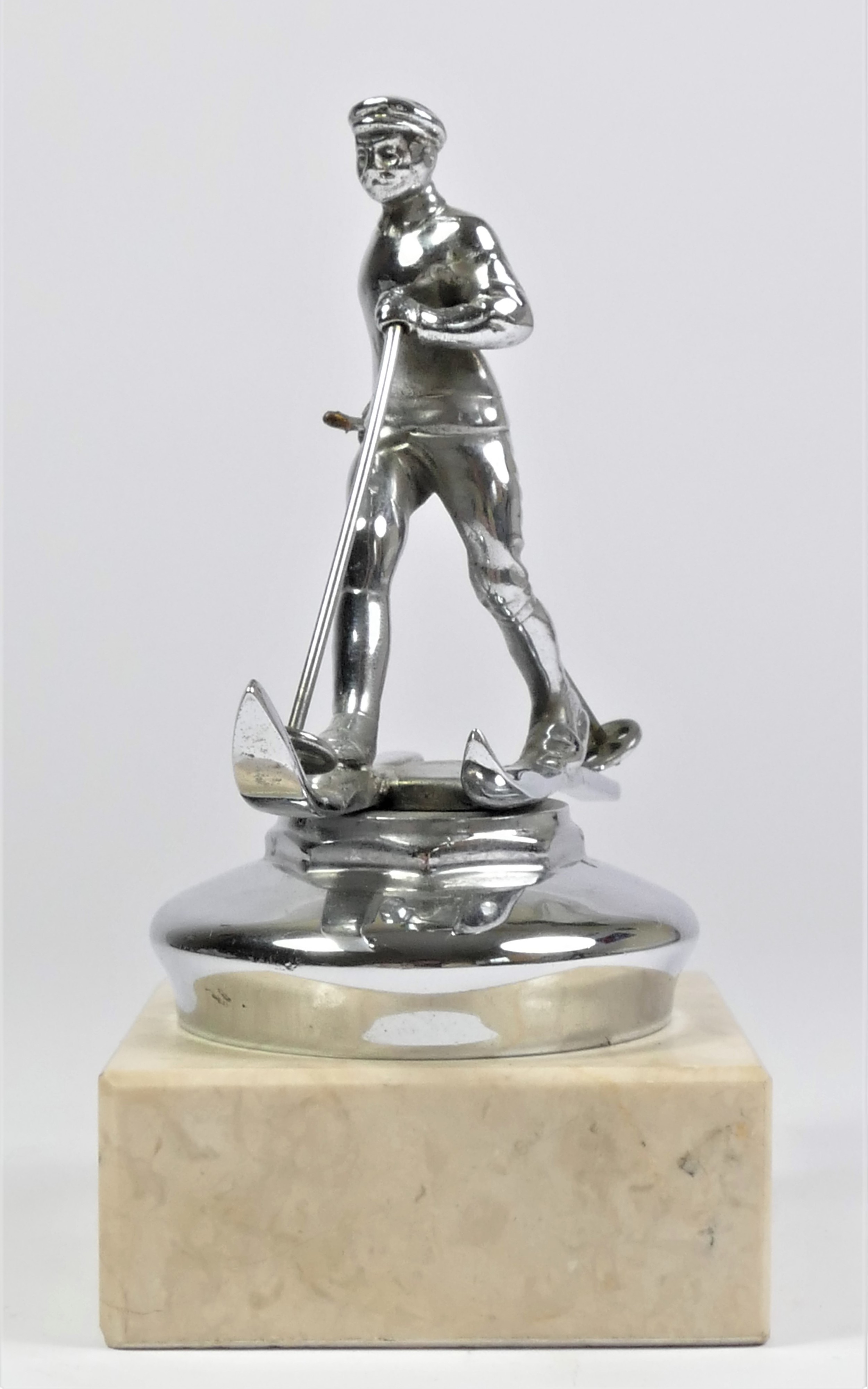 A chrome car mascot in the form of a skier mounted on a white onyx base, 15cm.