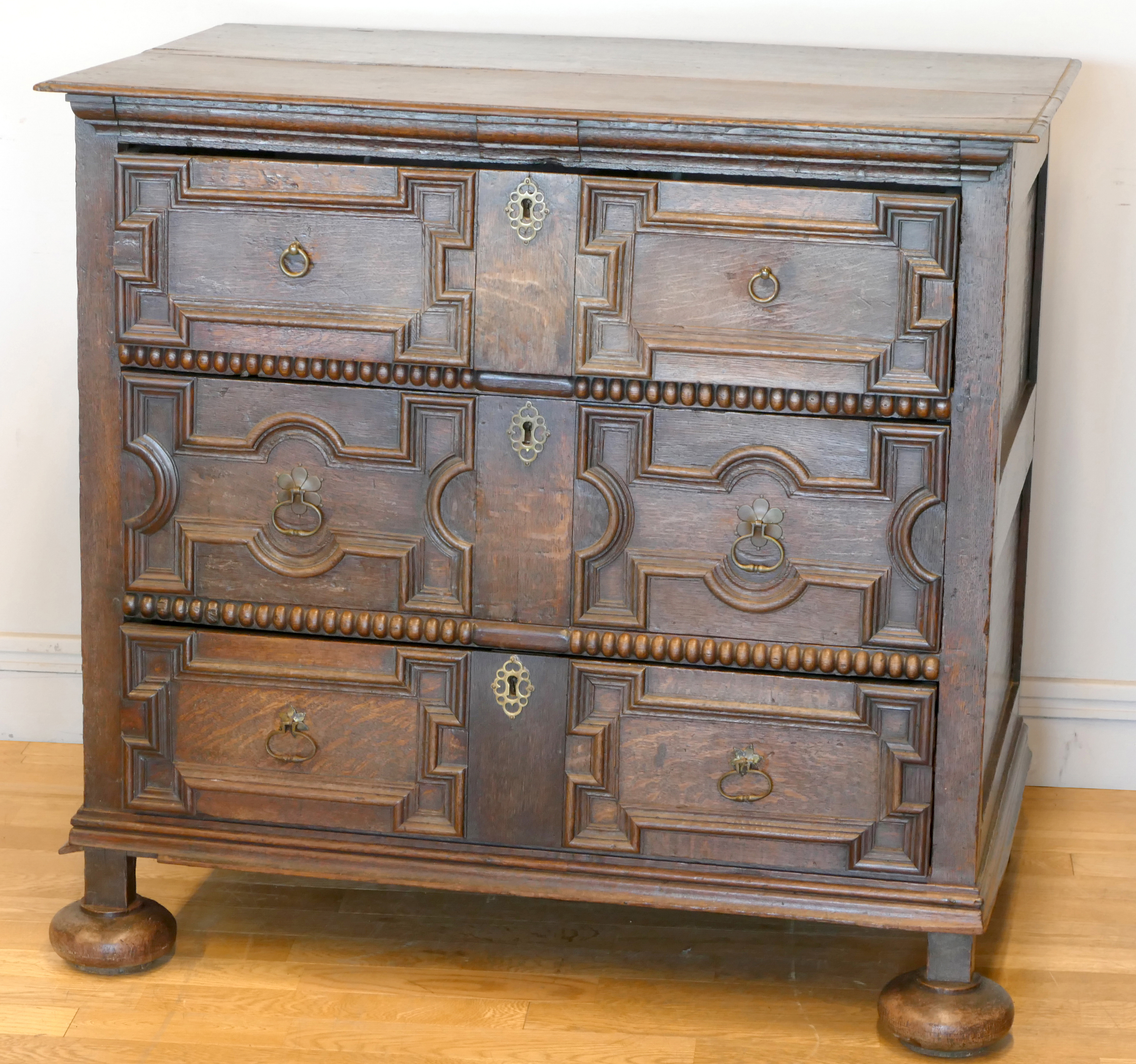 A late 17th century oak chest of three long drawers, two plank top over geometric moulded drawer