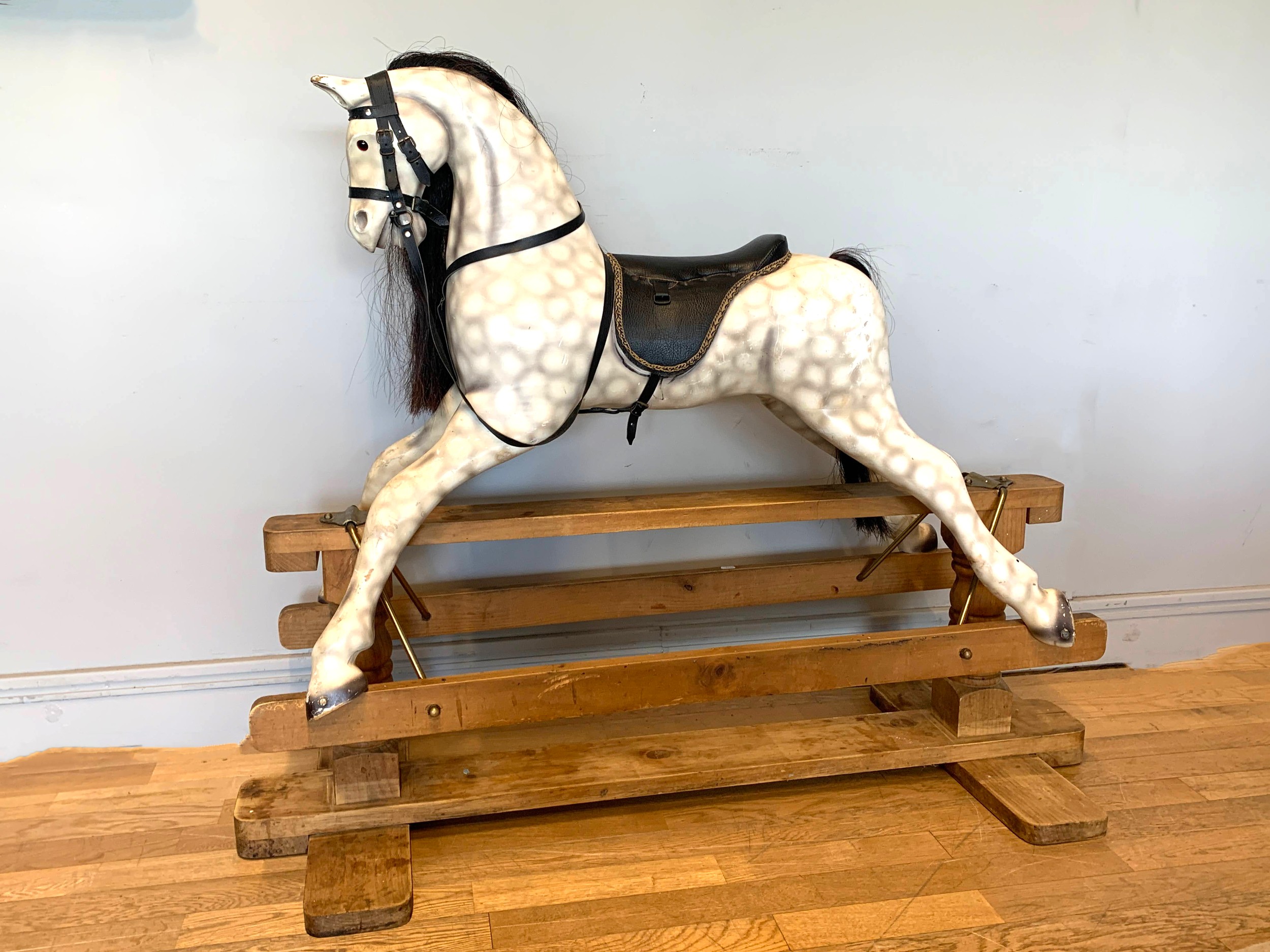 A large child's painted wood rocking horse, finished in a dapple grey with black leather saddlery,