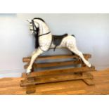A large child's painted wood rocking horse, finished in a dapple grey with black leather saddlery,