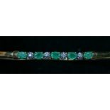 A 9ct gold emerald and diamond line bangle, internal 18cm, 4.6gm
