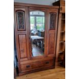 An Edwardian walnut wardrobe with mirrored door flanked by carved floral panels over a single