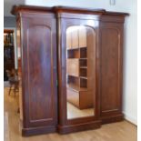 A Victorian mahogany breakfront triple wardrobe with central mirror panel door enclosing linen