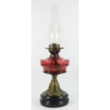 Victorian brass oil lamp with cranberry glass globe, raised on a ceramic base - 58cm tall.