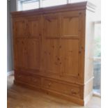A substantial modern pine triple wardrobe having four paneled doors over two long drawers below - W: